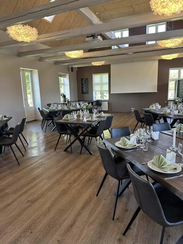 Salen med plankeborde, sorte stole og store vinduer ud mod golfbanen